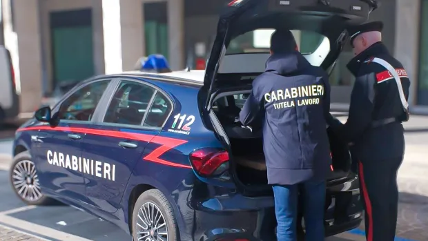 Carabinieri, uno con la giacca della Tutela lavoro, accanto a un'auto di servizio